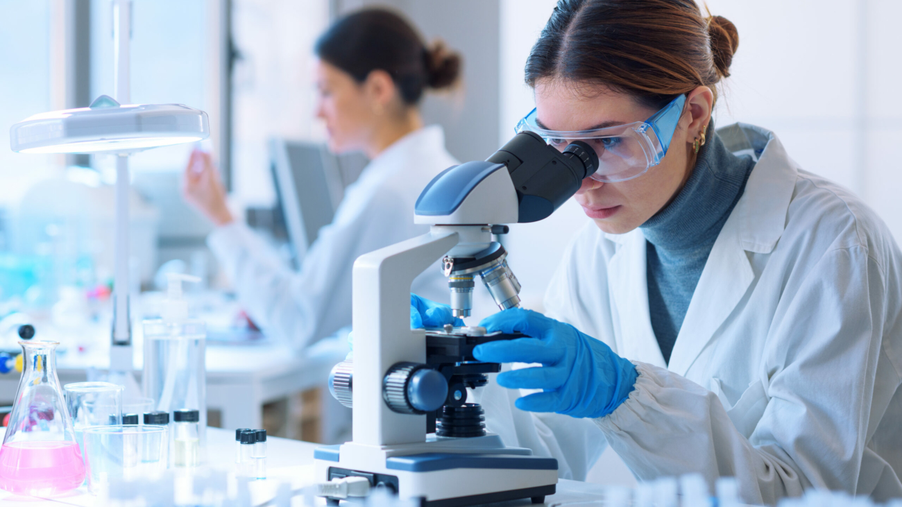 Young scientists conducting research investigations in a medical laboratory, a researcher in the foreground is using a microscope