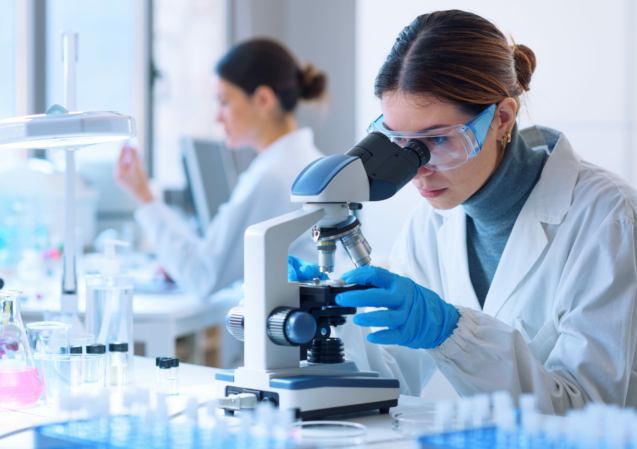 Young scientists conducting research investigations in a medical laboratory, a researcher in the foreground is using a microscope